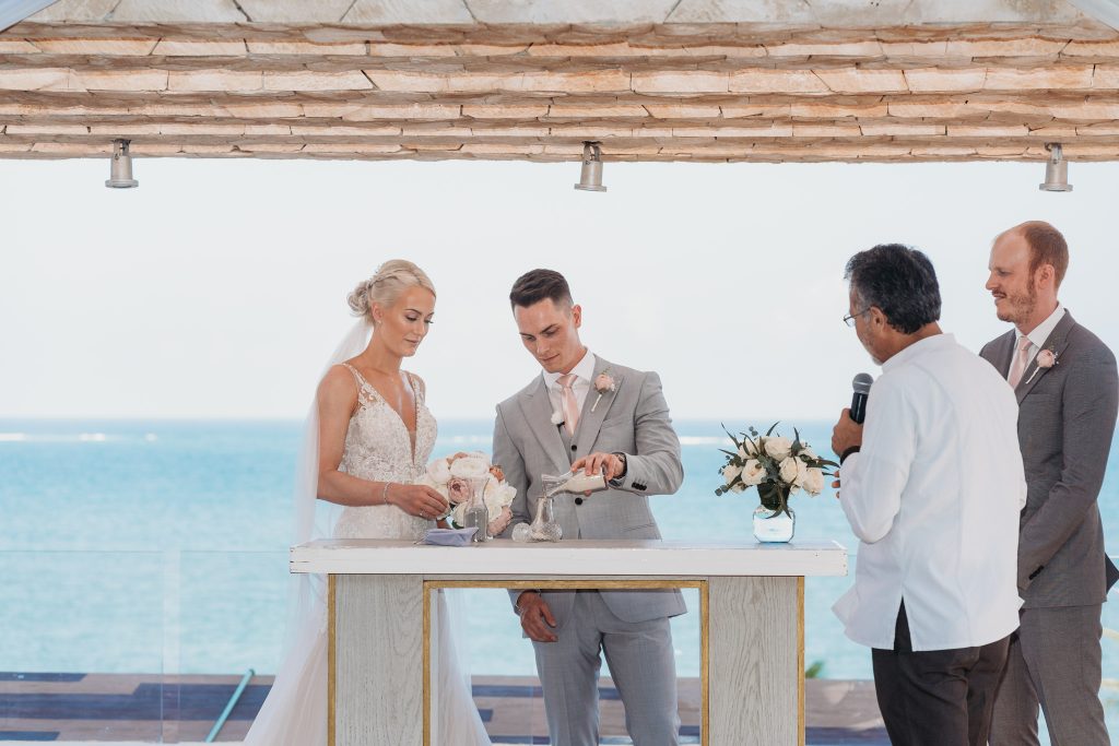Bride and groom perform sand ceremony with the sea behind them