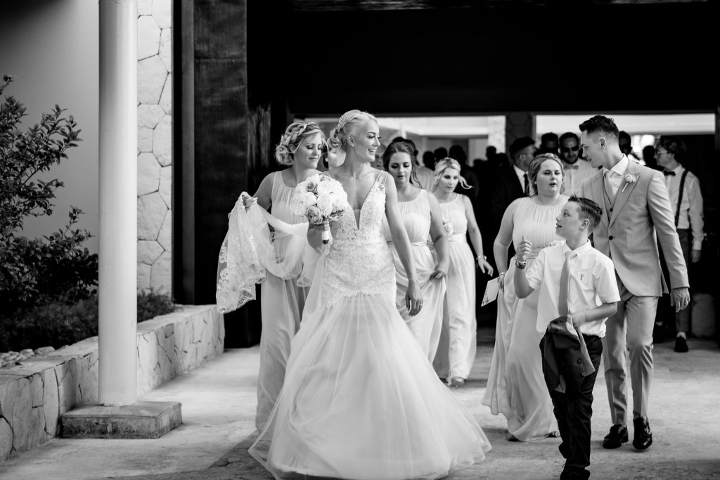 Black & white photo of Bride walking to the beach with her wedding party and page boy