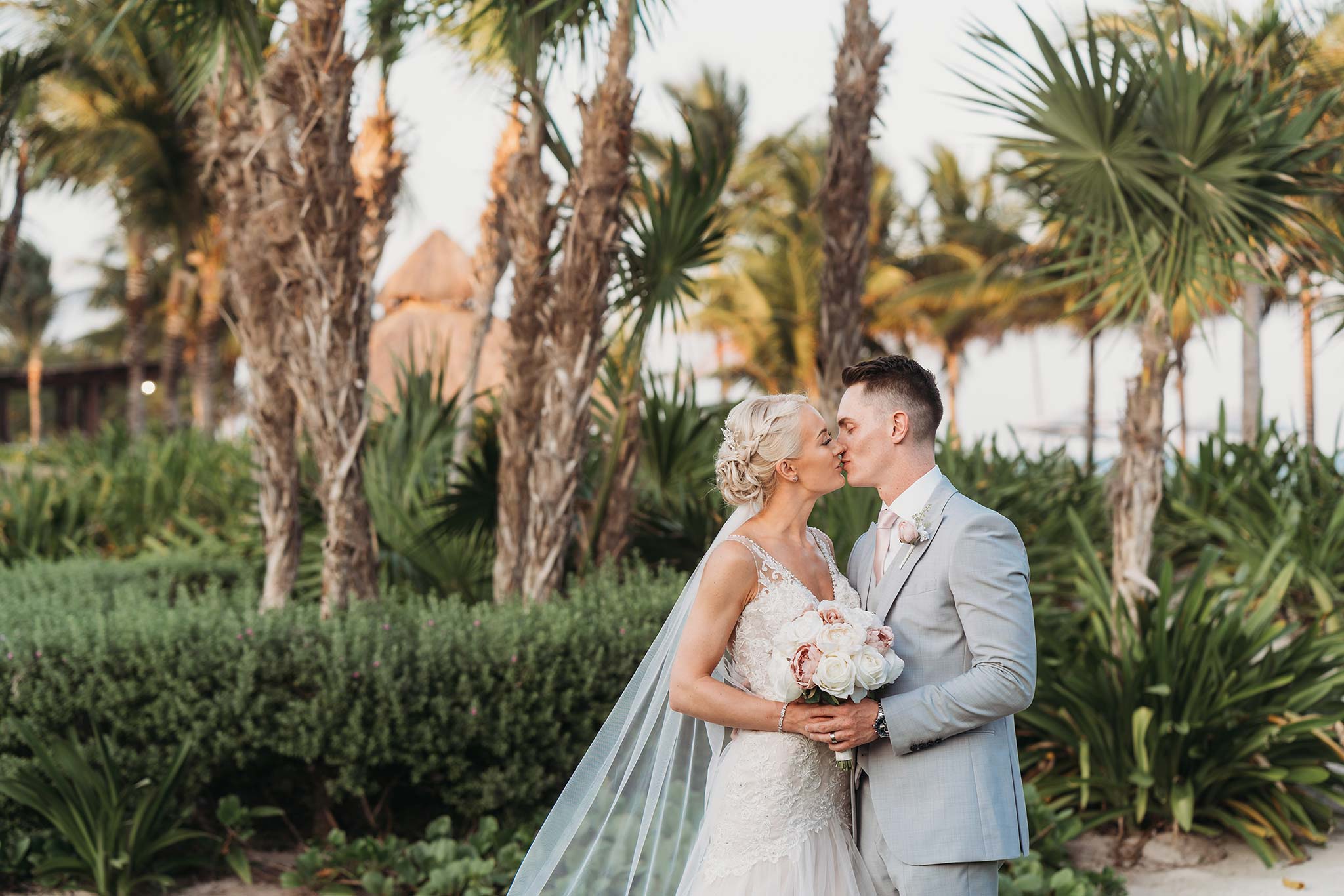 Royalton Riviera wedding photos - Bride & groom kissing with palm trees behind them