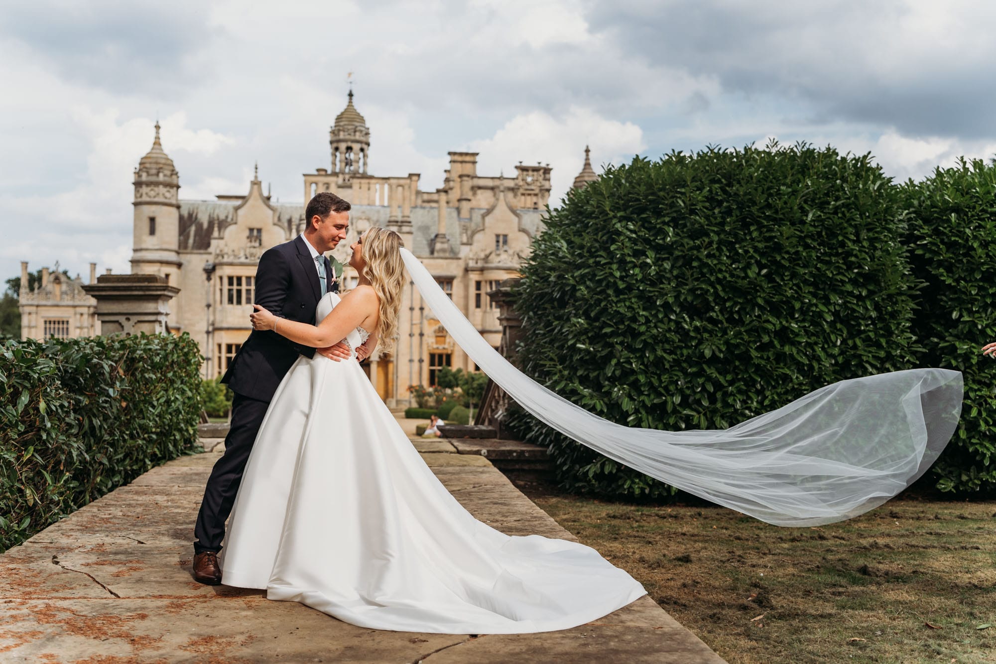 Bride holding her veil blowing in the wind whilst stood at the gates of Harlaxton Manor