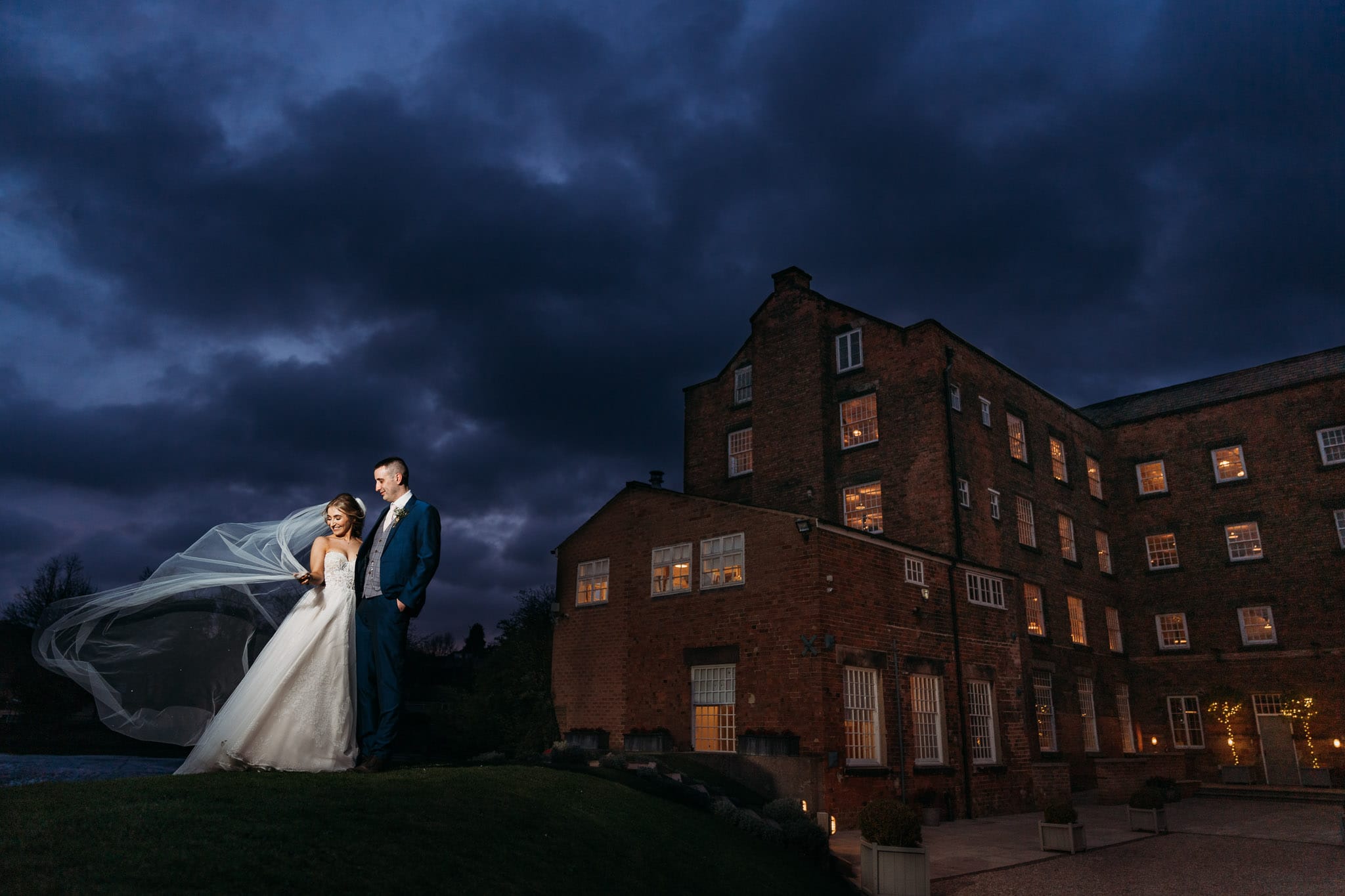 Beautiful evening portrait of bride & groom outside west mill with veil flowing as wind blows it