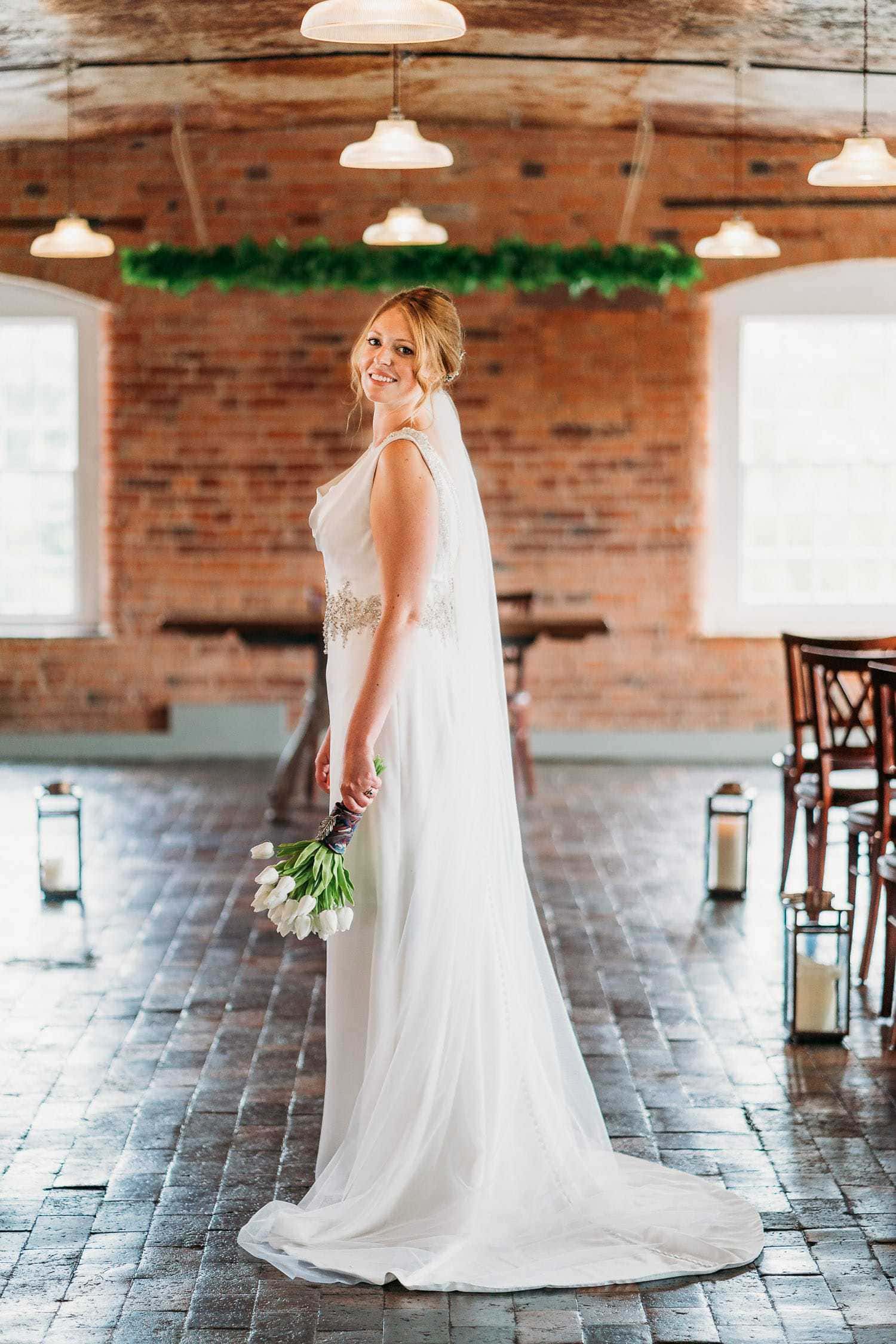 Beautiful bride standing in ceremony room at West Mill holding her bouquet